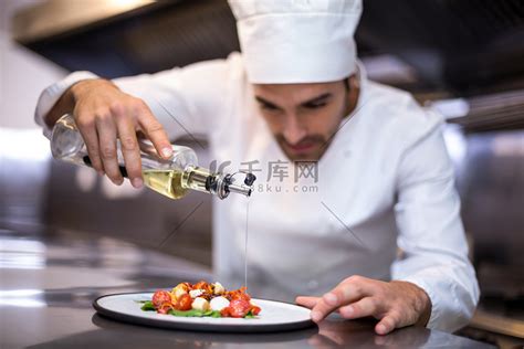 英俊的厨师把橄榄油倒在饭菜上高清摄影大图-千库网