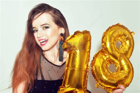 一个18岁生日的女孩带着金色的数字气球兴奋的十八女孩与绿色化妆和黑色礼服微笑模型庆祝和玩乐很可爱的高清图片下载-正版图片502524576-摄图网