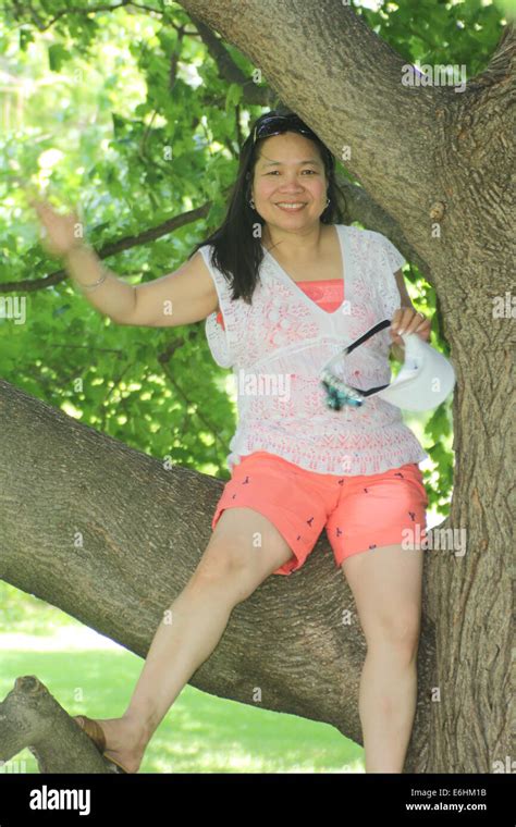 Mature Asian woman wearing shorts, sitting on a large branch of a big ...