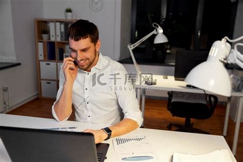 业务、加班、最后期限和人的概念-快乐的商人，在夜间办公室用电脑打电话给智能手机。高清摄影大图-千库网