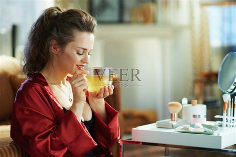 在阳光明媚的日子里，女人在现代的客厅里喝着绿茶照片摄影图片_ID:352952379-Veer图库