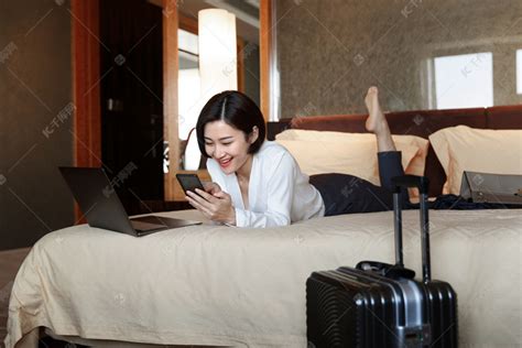 年轻女人趴在床上看手机高清摄影大图-千库网
